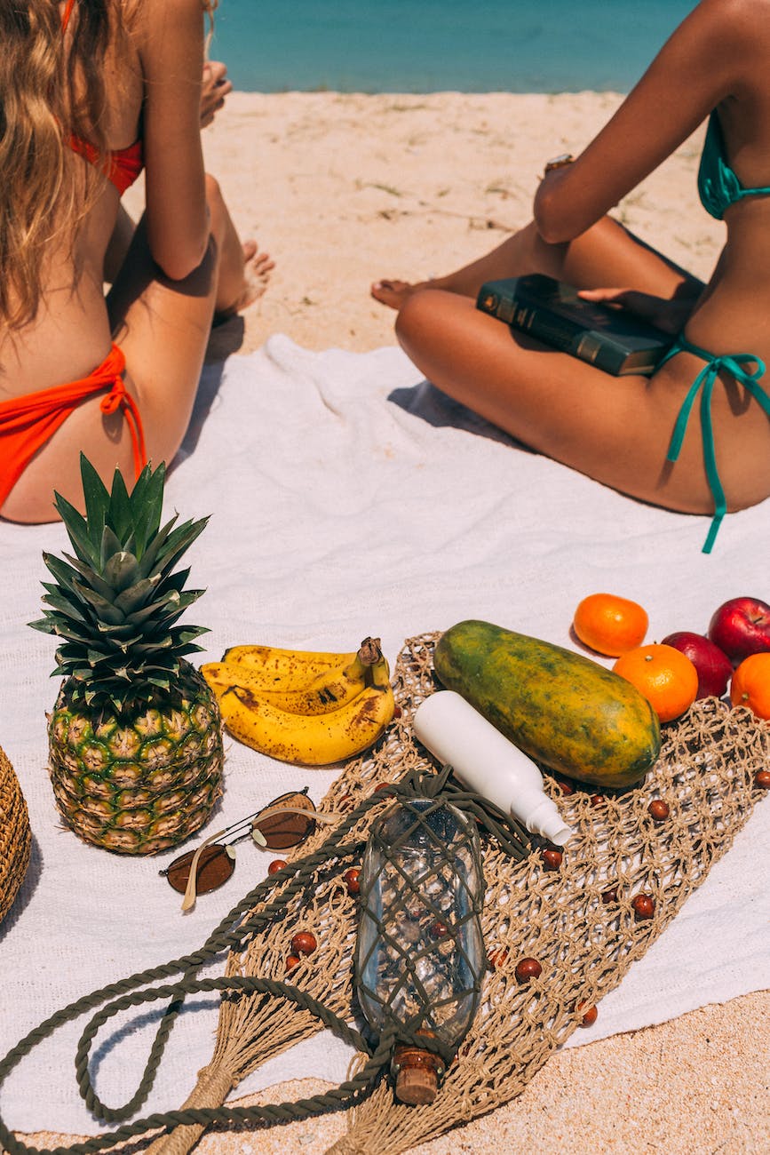 fruit and women sitting on towel on beach